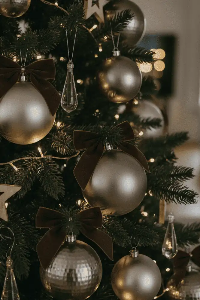 Close-up of a Christmas tree decorated with matte pewter baubles, espresso velvet bows, and warm white fairy lights